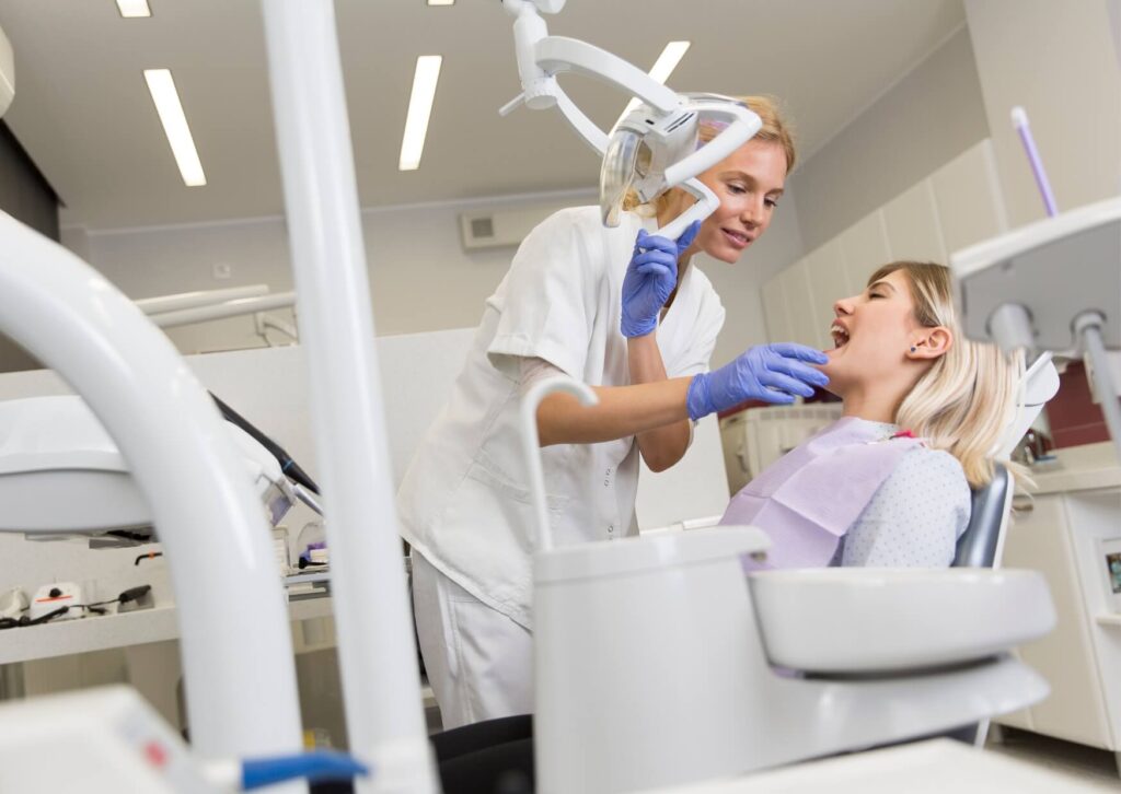 Dentist examining a patient's teeth before treatment, explaining factors that affect porcelain veneers longevity and maintenance over time.