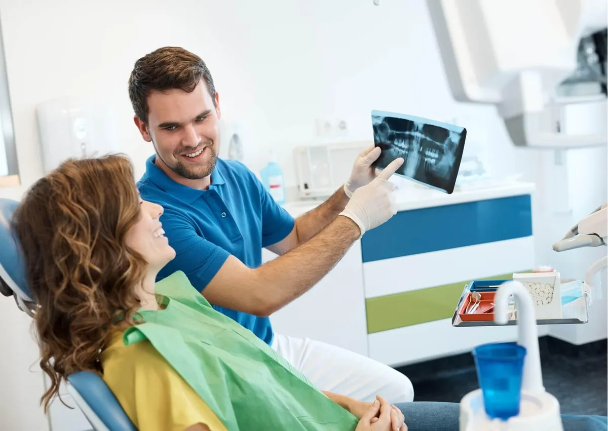 Dentist reviewing a dental X-ray with a patient while discussing an implant-supported bridge for replacing missing teeth.