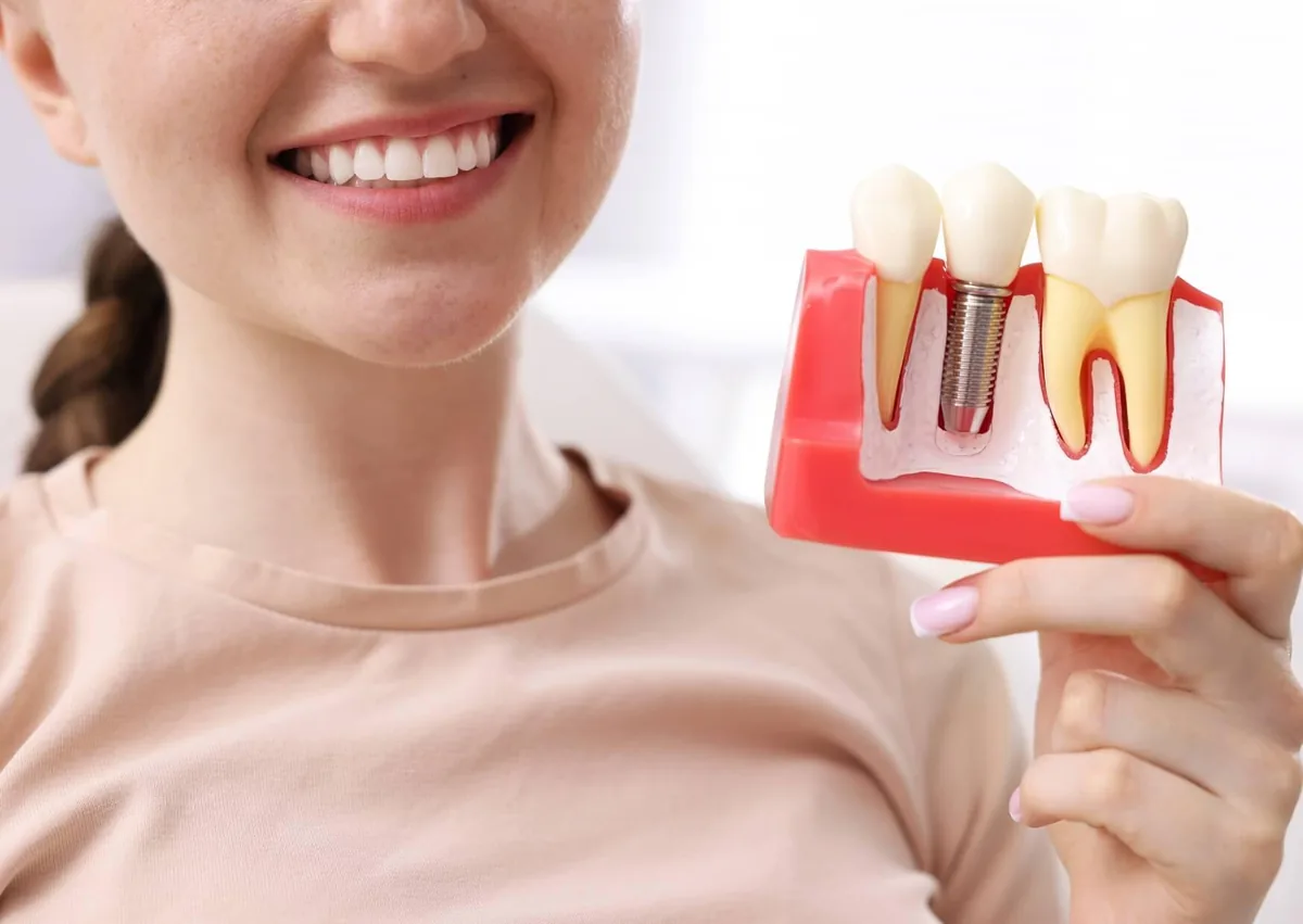 Patient holding a dental model showing a single-tooth implant as one of the common types of dental implants.