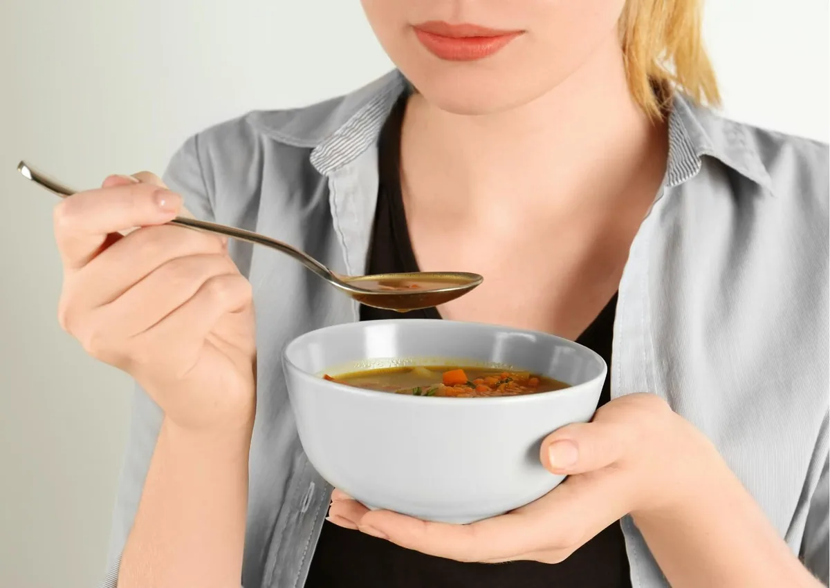 Patient eating soft soup as part of a recommended diet after dental implant surgery.